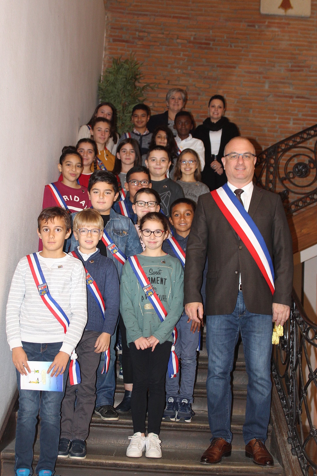 Les membres du Conseil Municipal des jeunes en compagnie du maire dans les escaliers de la mairie de Castelsarrasin. Ils portent tous une écharpe tricolore